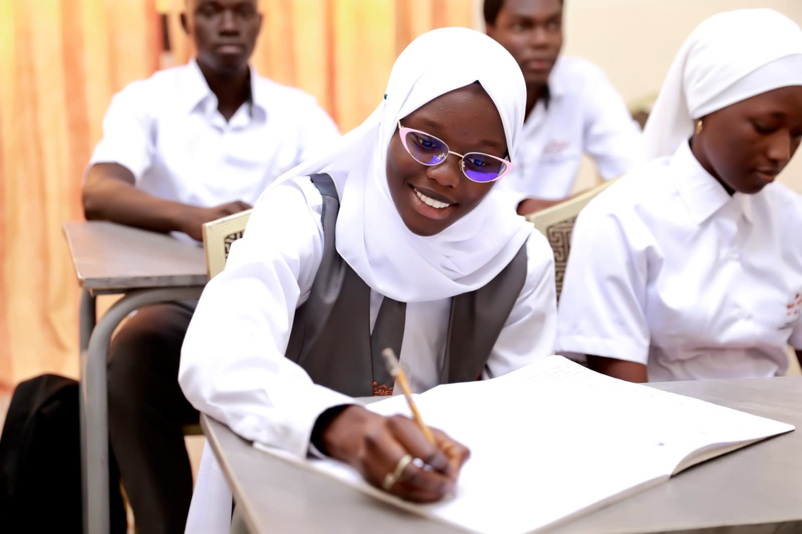 Une étudiante d’EHCT-Sahel sourit en prenant des notes, entourée de sa classe